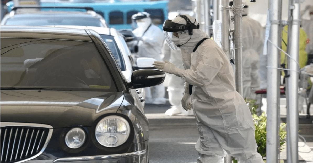 A worker in a hazmat suit approaching a car at a security checkpoint